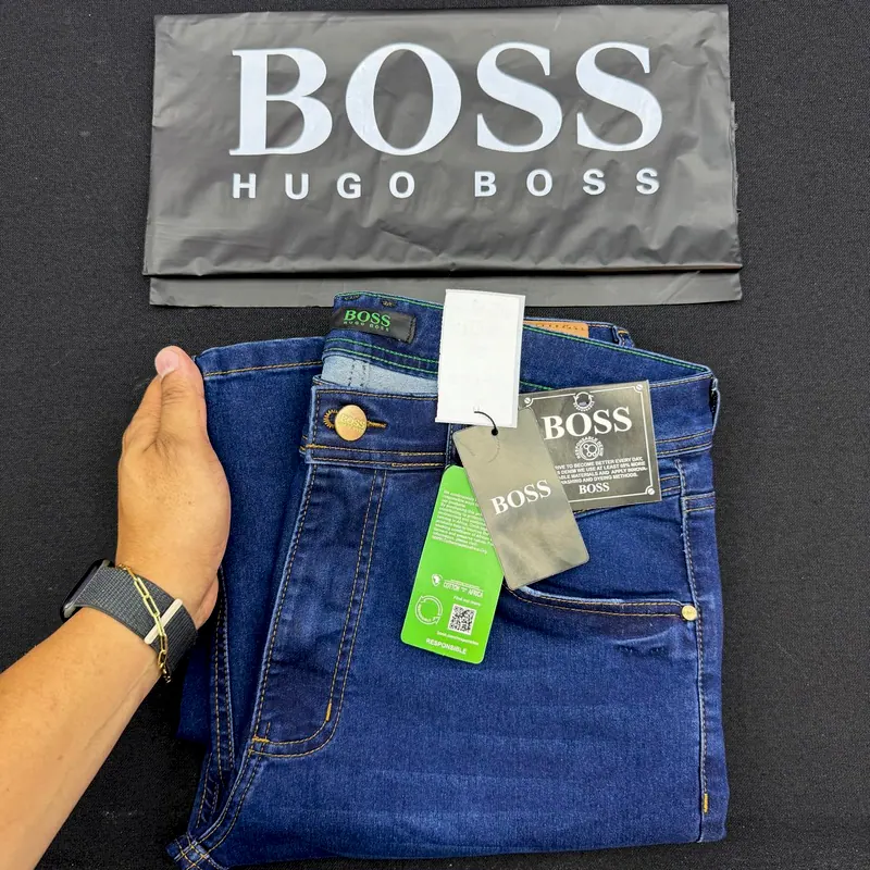 Calça jeans Boss azul-escura dobrada na mão, com as etiquetas e a sacola Hugo Boss