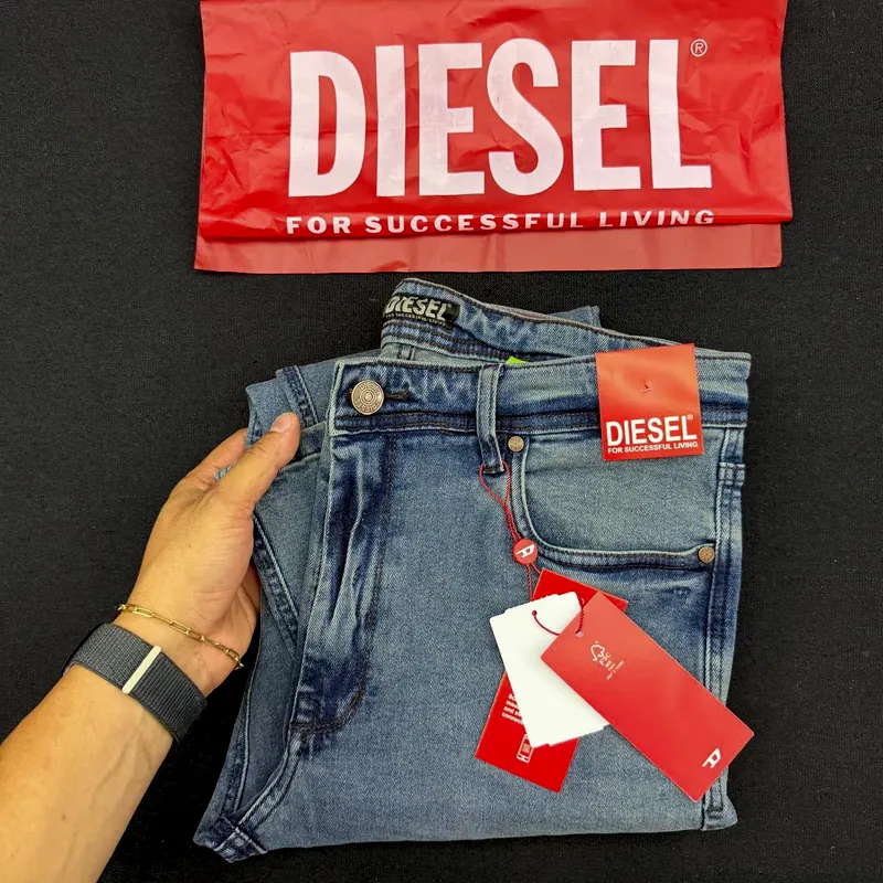 Calça jeans Diesel azul média dobrada na mão, com as etiquetas vermelhas e a sacola da marca